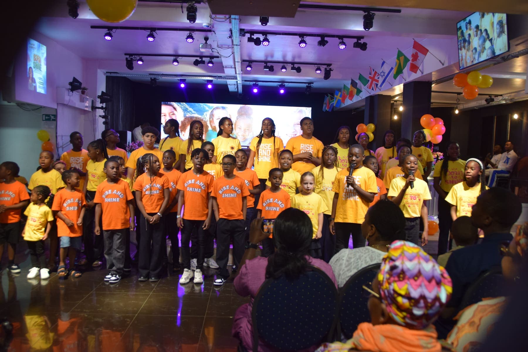 The children’s choir standing together on stage in orange and yellow shirts
