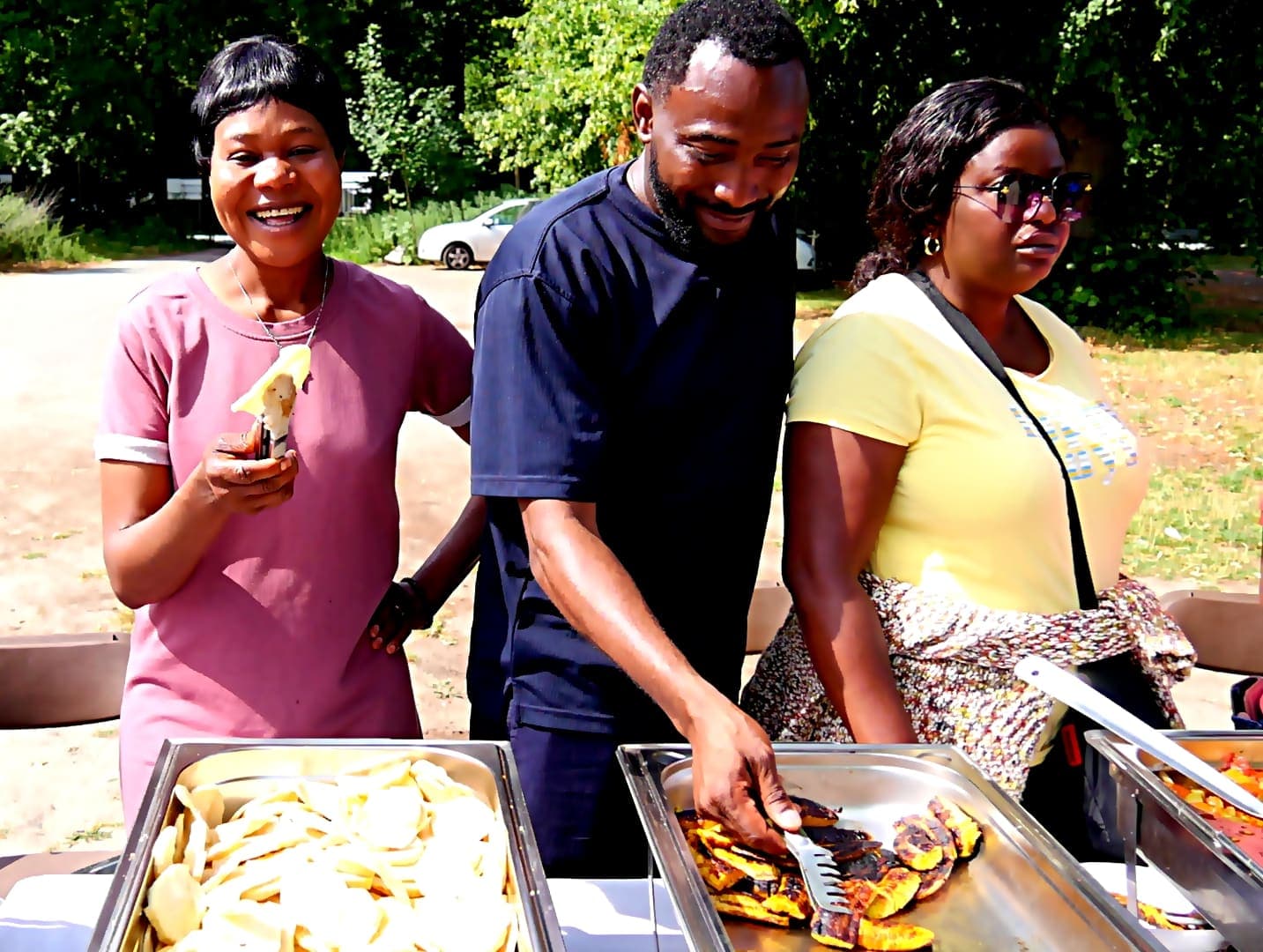 Three members serving food from trays at the barbecue